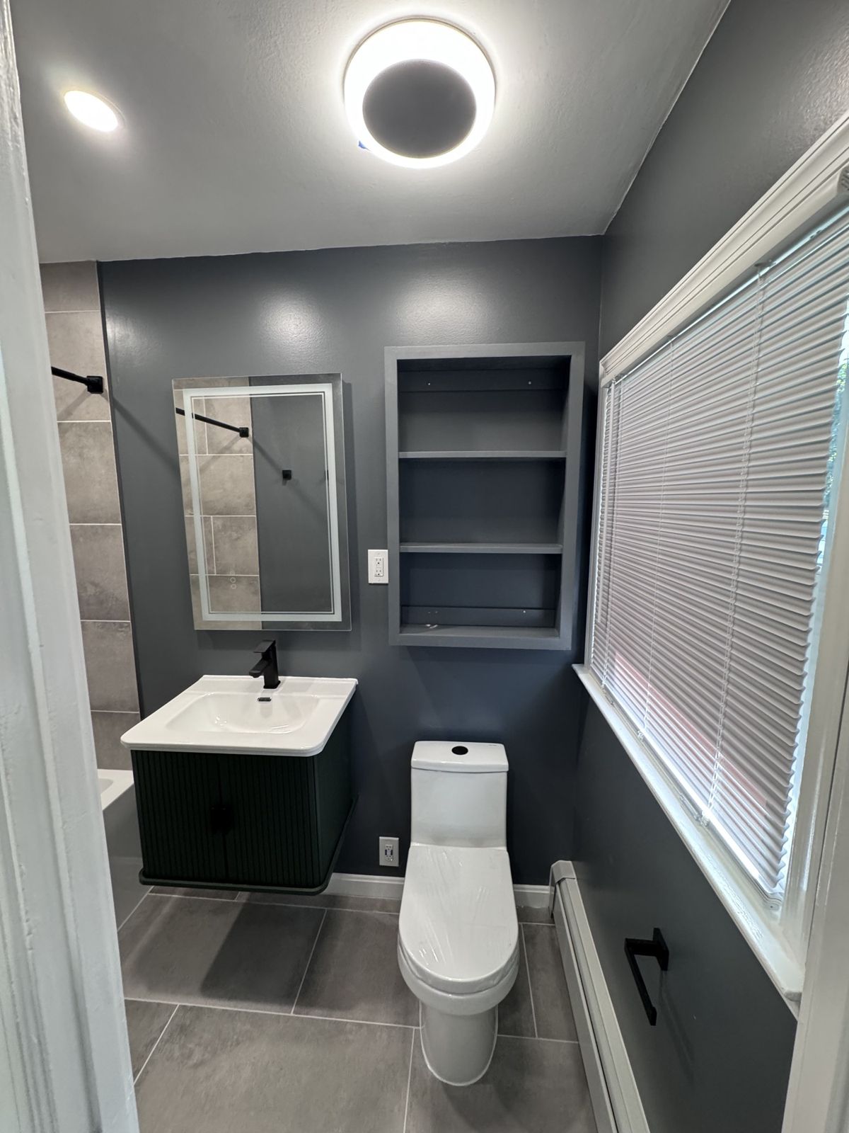 The same bathroom finished with dark walls, gray tile, a black vanity and built-in shelves