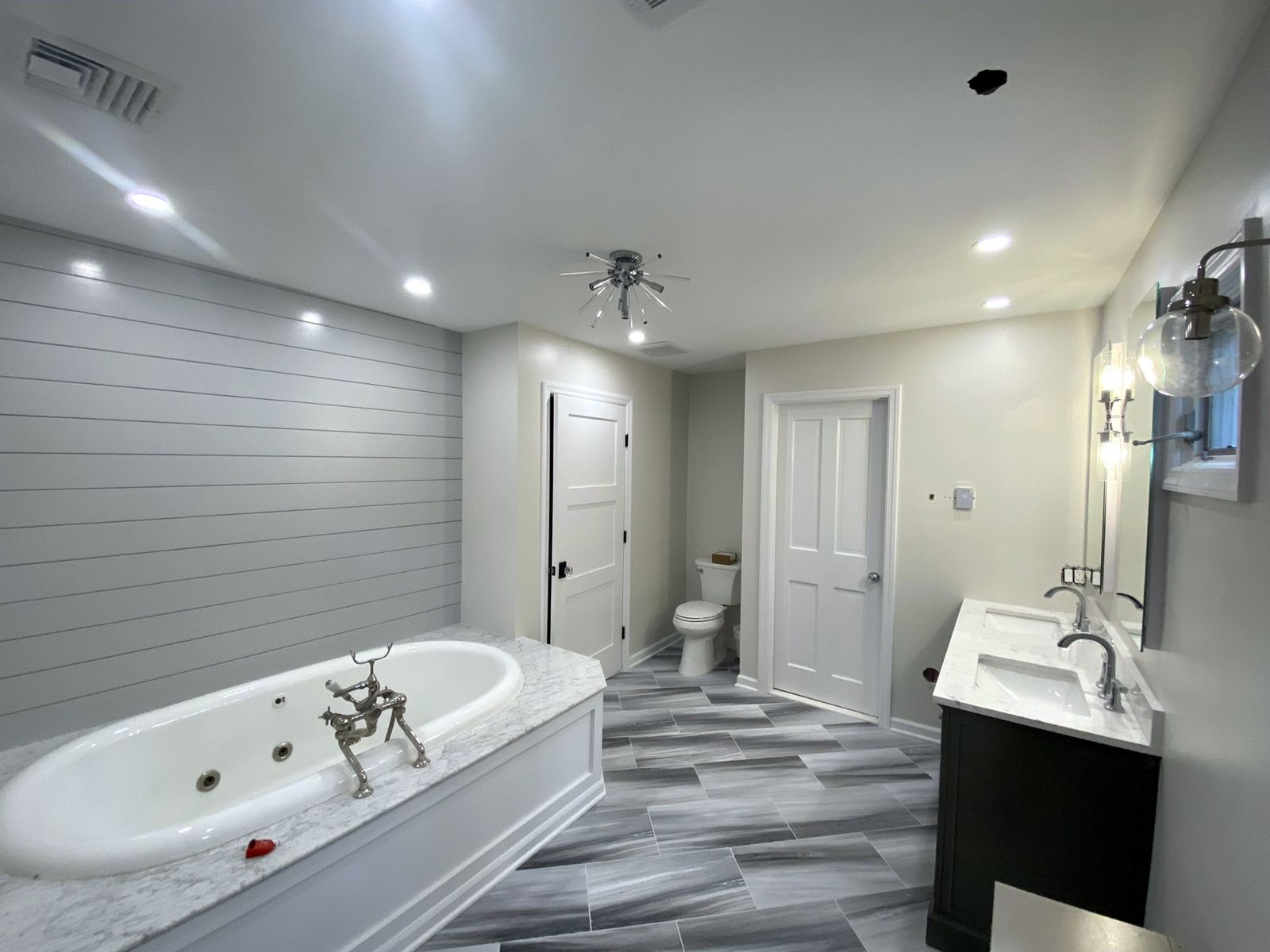 Finished primary bathroom with a shiplap accent wall, paneled whirlpool tub with marble deck, starburst light and wood-look tile floor