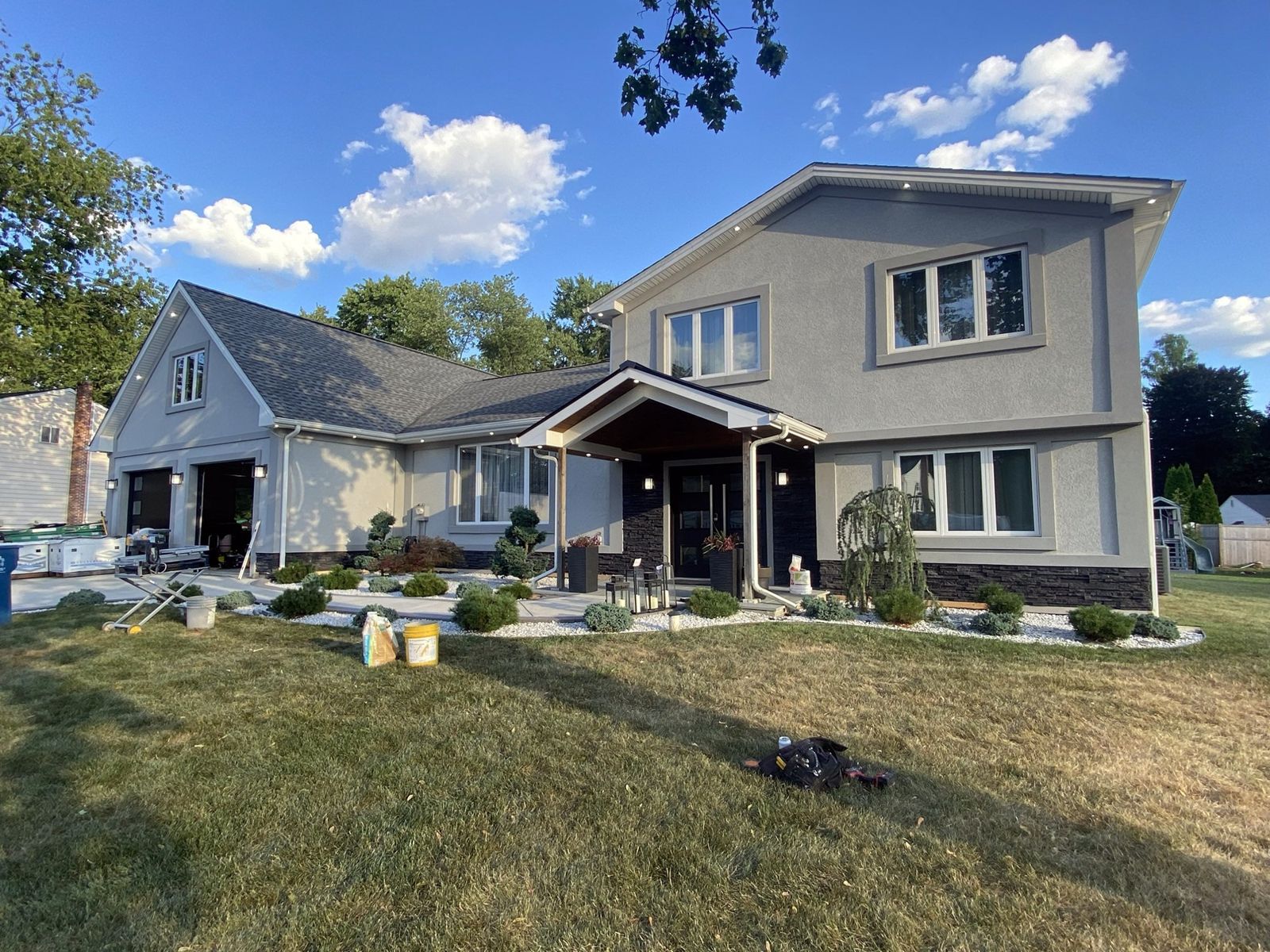 Renovated two-story home with gray stucco, a dark stacked-stone base, a covered entry porch and new landscaping