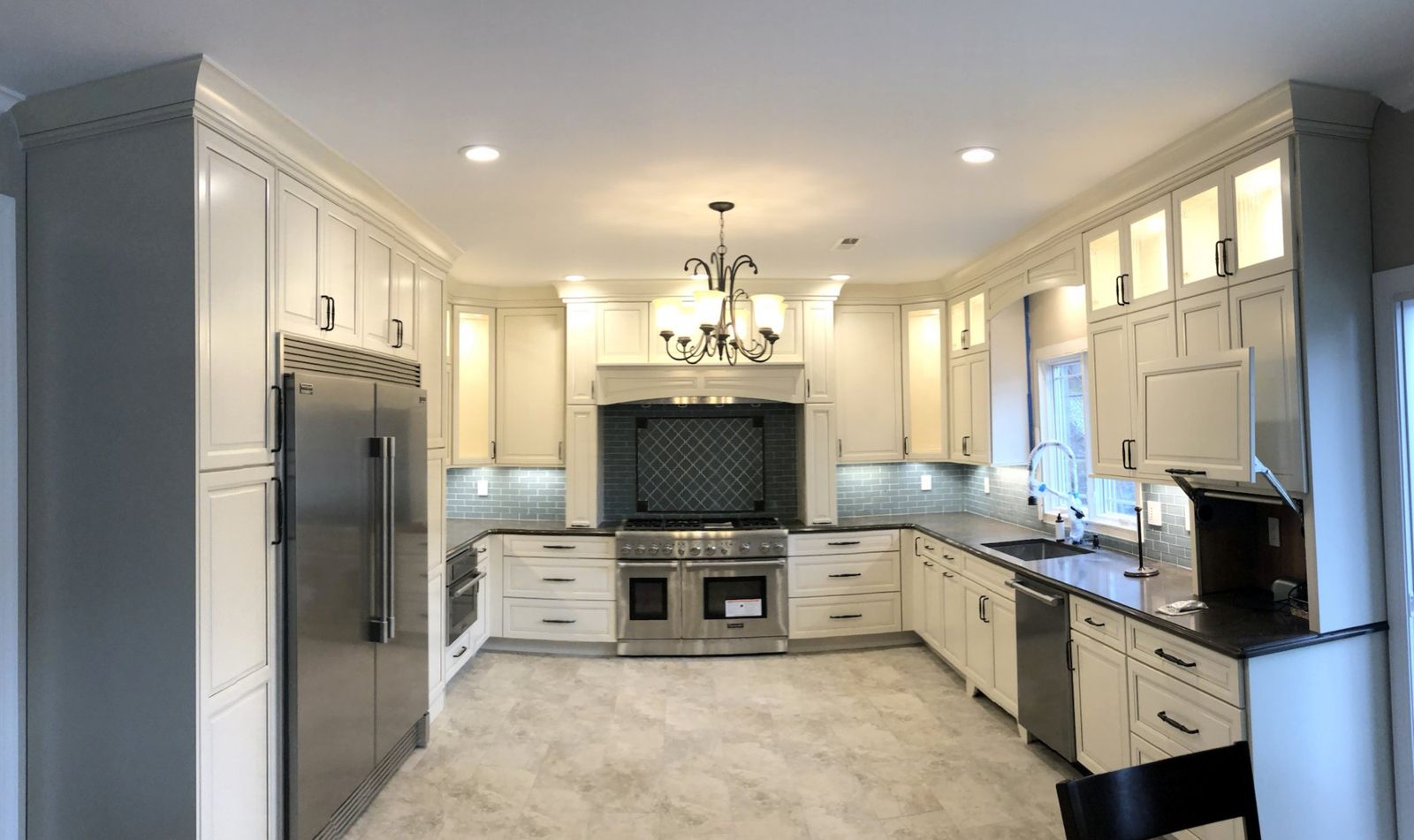 Finished white kitchen with crown-molded cabinets to the ceiling, lighted glass uppers, a glass tile backsplash and a stainless range